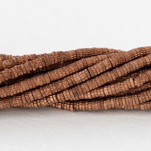 May include: A close-up of a strand of copper-colored beads. The beads are small and round, with a slightly textured surface. They are arranged in a loose, overlapping pattern.