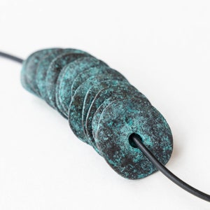 May include: A necklace with a series of stacked, round, teal-colored metal beads. The beads have a distressed, aged look and are strung on a black cord.