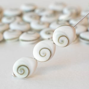 May include: Three white oval-shaped seashells with a brown and green spiral pattern. The shells are strung on a silver wire.