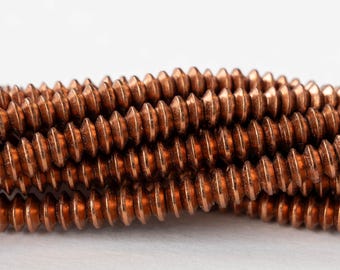 May include: A close-up of a strand of copper-colored beads. The beads are small and round, with a slightly textured surface. They are arranged in a spiral pattern.