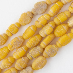 May include: Close-up of strands of yellow beads with a slightly textured surface. The beads have an oblong shape with a segmented design. The beads are strung together, creating a repeating pattern. The background is plain white.