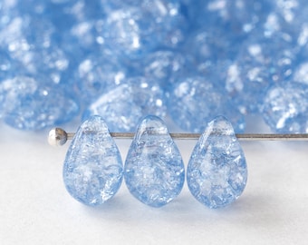 May include: Three light blue glass teardrop beads with a textured, crackled finish. The beads are strung on a silver wire.