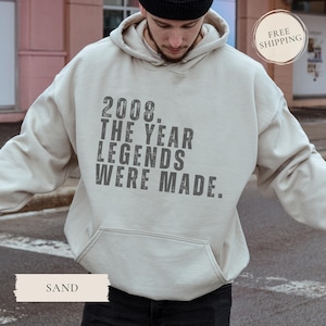 May include: Sand-colored hoodie with a front pocket and a drawstring hood. The front of the hoodie features the text "2008. THE YEAR LEGENDS WERE MADE." The word "SAND" is printed at the bottom of the image.