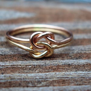 May include: A gold and rose gold ring with a knot design. The ring is made of wire and is a simple, elegant piece of jewelry.