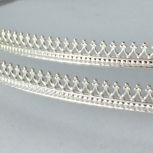 Puede incluir: Dos piezas de moldura de metal plateado con un borde festoneado decorativo.