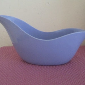 May include: A light blue plastic pitcher with a curved spout and a wide base. The pitcher is designed to hold liquids and has a smooth, glossy finish.