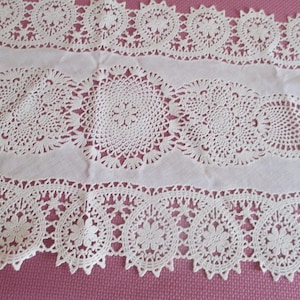May include: White crocheted lace table runner with a delicate floral pattern. The runner has a scalloped edge and is perfect for adding a touch of elegance to any table.