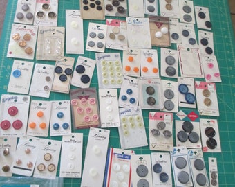 May include: A large collection of vintage buttons in various colors, sizes, and materials. The buttons are arranged on cards and in a jar. Some of the buttons have text on them, such as "Lansing" and "La Petite".