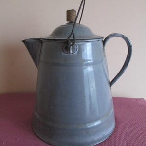 May include: A vintage blue enamel teapot with a wire handle and a cork lid. The teapot has a rounded body and a spout on one side.