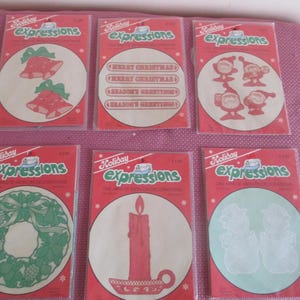 May include: Six packages of Holiday Expressions die-cut iron-on decorations. The packages feature a variety of designs, including bells, Christmas greetings, a wreath, a candle, and snowmen.