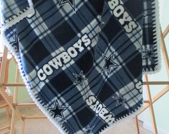 Op de afbeelding: Een blauwe en witte fleece deken met een ruitpatroon en het woord "COWBOYS" erop. De deken heeft een witte gehaakte rand.