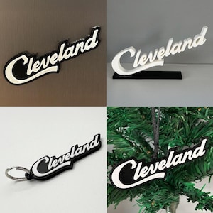 May include: A collection of Cleveland-themed items. Includes a black and white magnet, a white 3D-printed sign on a black base, a keychain, and a Christmas tree ornament. All items feature the word "Cleveland" in a stylized font.