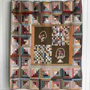 Puede incluir: Un edredón hecho a mano con un diseño de patchwork. El edredón presenta una variedad de cuadrados de tela en tonos de marrón, rojo, verde y azul. El centro tiene cuatro cuadrados marrones con diseños de cestas.