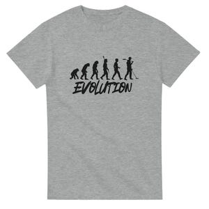 May include: A grey t-shirt featuring a black silhouette of the evolution of man, culminating in a man holding a metal detector. The text "EVOLUTION" is printed beneath the silhouettes.