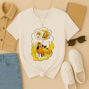 Peut inclure: T-shirt crème avec un dessin animé d'un chien dans une pièce en feu, tenant une tasse de café, avec la phrase "This is fine". Le chien porte un chapeau. Le t-shirt a un col rond et des manches courtes.