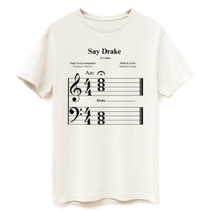 Könnte beinhalten: Weißes T-Shirt mit einem Notenblatt-Design, das das Lied "Say Drake" in A-Moll zeigt. Die Noten enthalten die Texte "Drake" und "Kendrick Lamar".