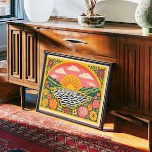 Peut inclure: Une affiche encadrée représentant un paysage vibrant. L'œuvre d'art présente un soleil stylisé se couchant sur une rivière ondulée, avec des fleurs et des montagnes colorées. La palette de couleurs comprend du rose, du jaune, du vert et du bleu.