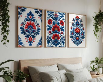 May include: Three framed floral art prints. Each print features a red and blue floral design on a white background. The frames are a light wood color. The art is displayed above a bed with white bedding.