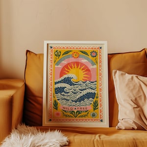 May include: A framed art print with a colourful illustration of a sun, waves, and the words "WILD FREE." The artwork is set against a yellow background with floral and rainbow elements, framed in white.