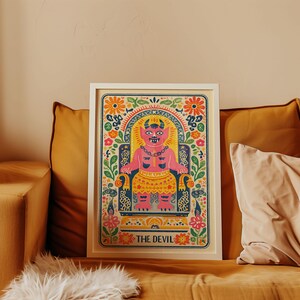 Könnte beinhalten: Ein gerahmter Kunstdruck mit einer rosa Teufelsfigur auf einem Thron, umgeben von floralen und dekorativen Mustern. Der Druck enthält den Text "THE DEVIL" am unteren Rand. Das Kunstwerk ist lebendig und farbenfroh.