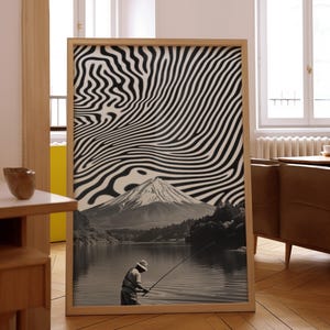 May include: A framed black and white abstract print with a mountain and a lake in the background. A person is fishing in the lake. The print is in a wooden frame.