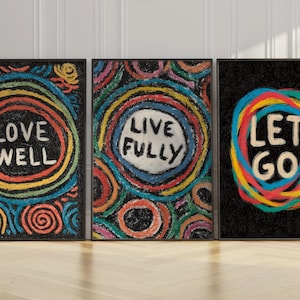 May include: Three framed art prints with black frames. Each print features colorful, abstract designs with the words "LOVE WELL", "LIVE FULLY", and "LET GO" in white. The art has a textured, crayon-like appearance.