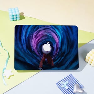 May include: A laptop skin featuring a surreal illustration of a figure with an Apple logo head emerging from a swirling tunnel of blue and purple hues. The figure wears a red jacket. The background is a mix of yellow, green, and blue.