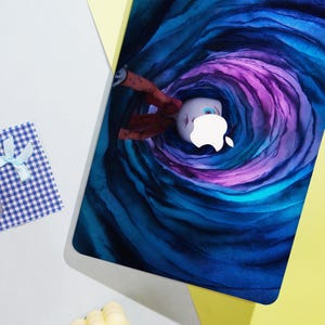 May include: A laptop skin featuring a whimsical illustration of a character falling into a swirling vortex of blue and purple hues. The Apple logo is integrated into the design. A small gift box with a blue and white checkered pattern is in the corner.