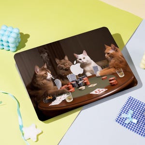 Könnte beinhalten: Laptop-Skin mit einem Pokerspiel mit vier Katzen. Die Katzen sitzen an einem Tisch mit Pokerchips, Karten und Getränken. Eine Katze raucht eine Zigarette. Das Apple-Logo ist auf dem Tisch zu sehen.