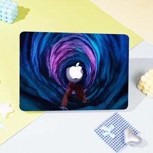 May include: A laptop skin featuring a stylized illustration of a figure with an Apple logo head, wearing a red jacket, in a blue and purple tunnel. The design is on a black rectangular surface.