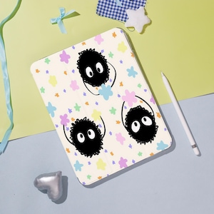 May include: A cream tablet case with three black, fluffy cartoon characters with large white eyes. The case is decorated with colourful star and flower shapes. A white stylus is positioned to the right of the case.