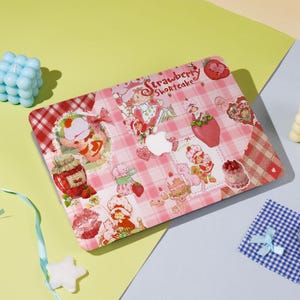Może przedstawiać: Różowa i biała kratka na laptopie z motywem Strawberry Shortcake. Skórka zawiera różne obrazy Strawberry Shortcake i jej przyjaciół, w tym truskawkę, słoik dżemu i ciasto.