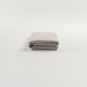 May include: A folded linen sheet in a light beige colour. The sheet is folded in thirds and is lying flat on a white surface.
