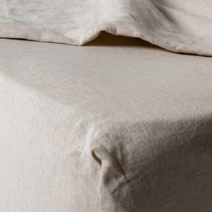 May include: A close-up of a natural linen fitted sheet. The sheet is a light beige colour and has a smooth, textured surface.