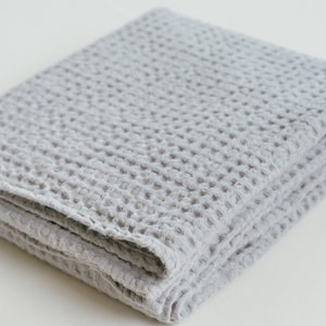 Peut inclure: Une couverture en tissu gaufré gris pliée sur une surface blanche. La couverture est faite d'un tissu doux et texturé.