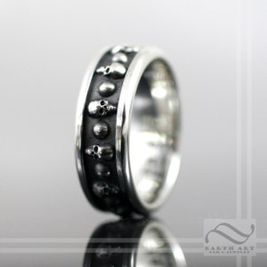 May include: A silver ring with a black skull design. The ring is made of sterling silver and has a polished finish.