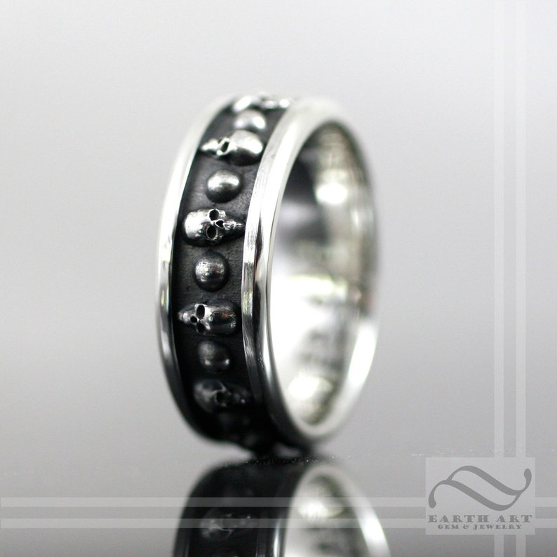 May include: A silver ring with a black skull design. The ring is made of sterling silver and has a polished finish.