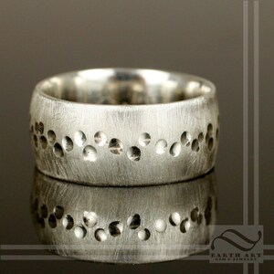 Può includere: Una fede nuziale in argento con una finitura testurizzata e una fila di piccoli punti in rilievo attorno al centro.