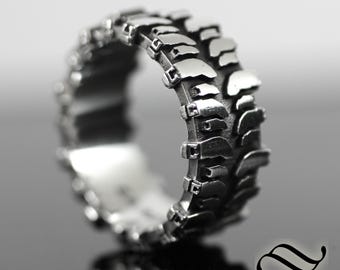 May include: A silver ring with a tire tread design. The ring is made of metal and has a detailed, realistic tire tread pattern.