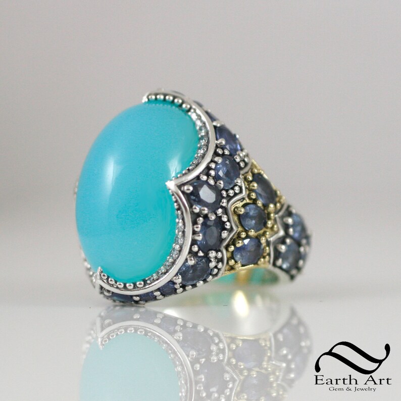 May include: A turquoise gemstone ring with a silver band and blue sapphire accents. The ring has a detailed design with gold accents.
