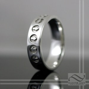 May include: A silver band ring with a series of arrows engraved around the band.