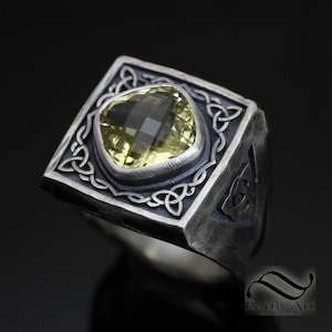 Puede incluir: Un anillo de plata con un diseño de nudo celta y una piedra preciosa amarilla en el centro.