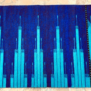 May include: A blue and turquoise woven rug with a geometric pattern. The rug has a fringe border.