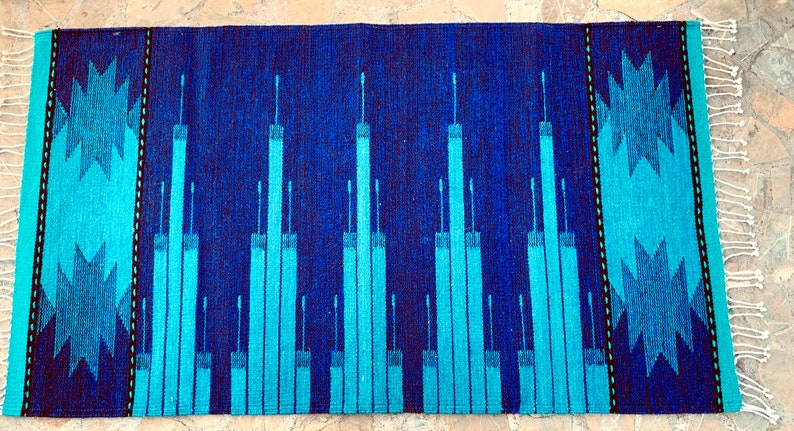 May include: A blue and turquoise woven rug with a geometric pattern. The rug has a fringe border.
