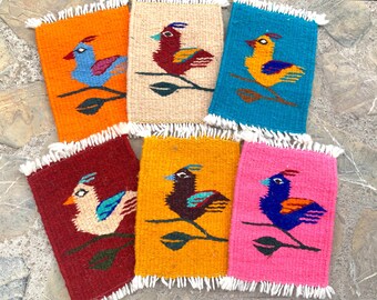 May include: Six colorful woven coasters featuring a bird design. The coasters are made of wool and have a fringed edge. The birds are depicted in various colors, including blue, red, yellow, and green.