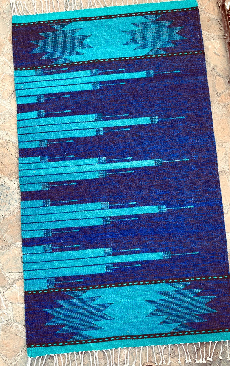 May include: A blue and turquoise patterned rug with a geometric design. The rug has a fringe border.