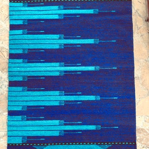 May include: A blue and turquoise woven rug with a geometric pattern. The rug has a fringe border.
