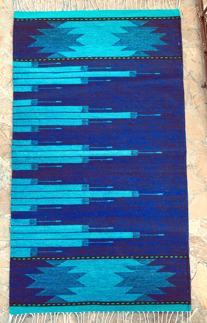 May include: A blue and turquoise woven rug with a geometric pattern. The rug has a fringe border.