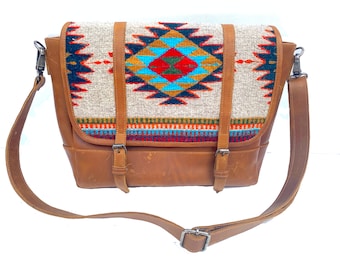 May include: A brown leather messenger bag with a colorful woven pattern on the front flap. The bag has a long adjustable strap and a buckle closure.