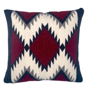 May include: A decorative pillow with a geometric pattern in shades of burgundy, black, white, and gray. The pillow has a diamond shape in the center and a border around the edges.